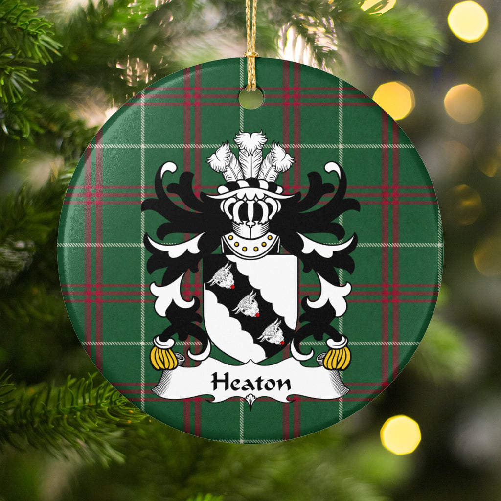 Heaton ornament hanging in a Christmas tree with warm lights; three white bull heads on a scalloped black diagonal band across a white shield on Welsh national tartan.