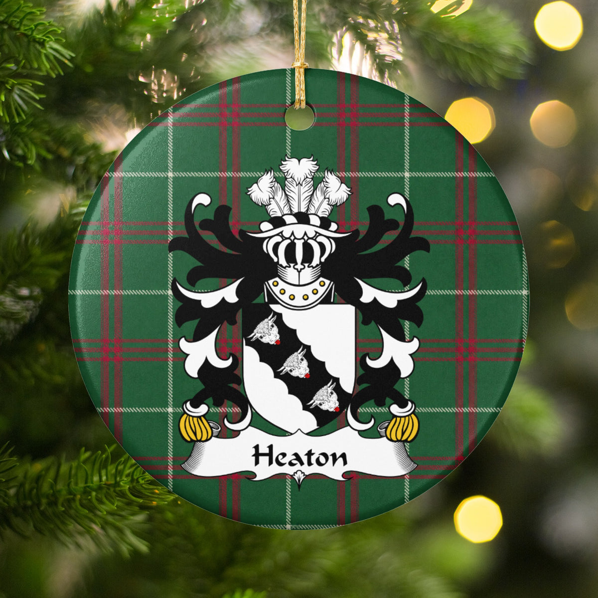 Heaton ornament hanging in a Christmas tree with warm lights; three white bull heads on a scalloped black diagonal band across a white shield on Welsh national tartan.