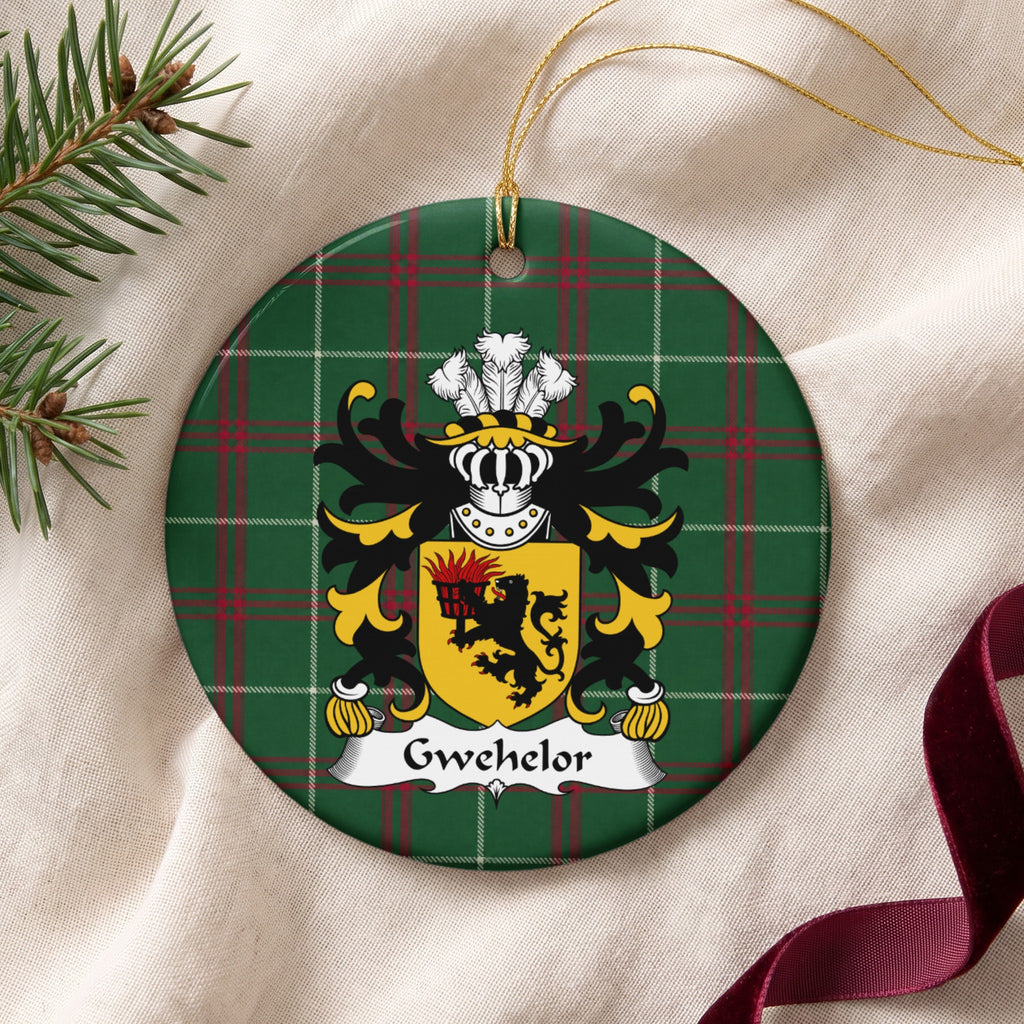 Gwehelor ornament on cream fabric beside evergreen and burgundy ribbon, with gold string; a black lion holding a flaming basket on a gold shield.