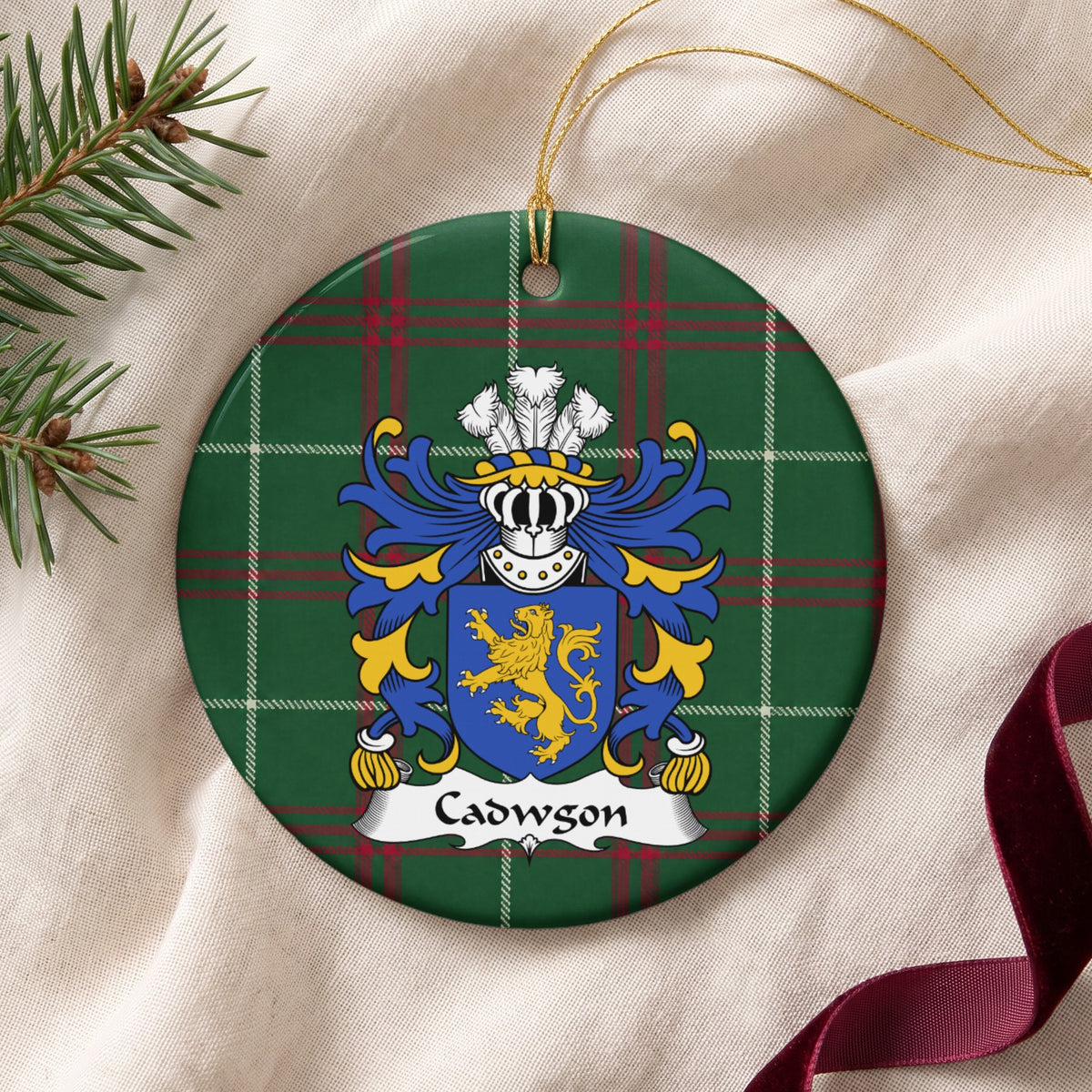 Cadwgon Style 2 ornament on cream fabric with gold string, evergreen and burgundy ribbon; a gold upright lion on a blue shield on Welsh national tartan.
