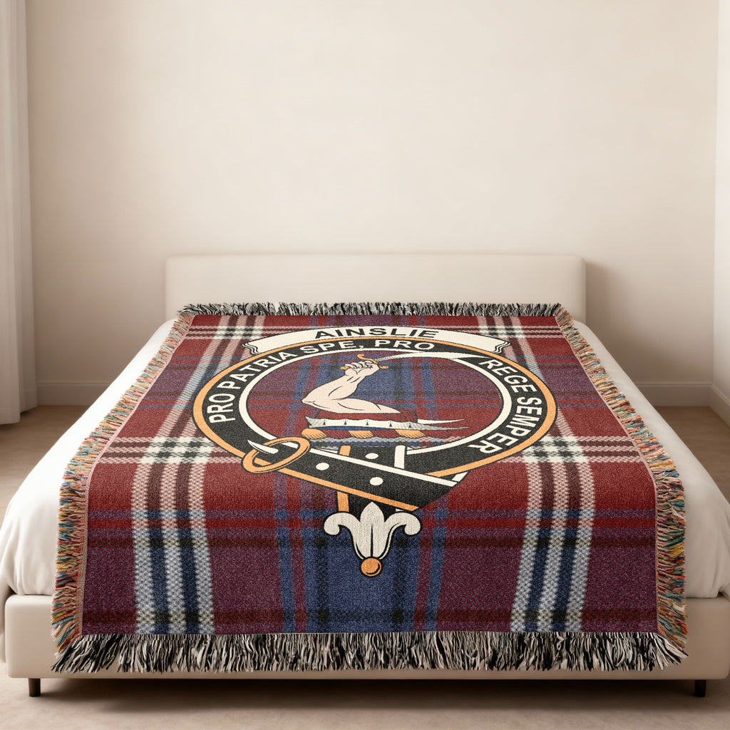 Ainslie Scottish woven blanket spread across a bed, showing the full crest design and tartan background