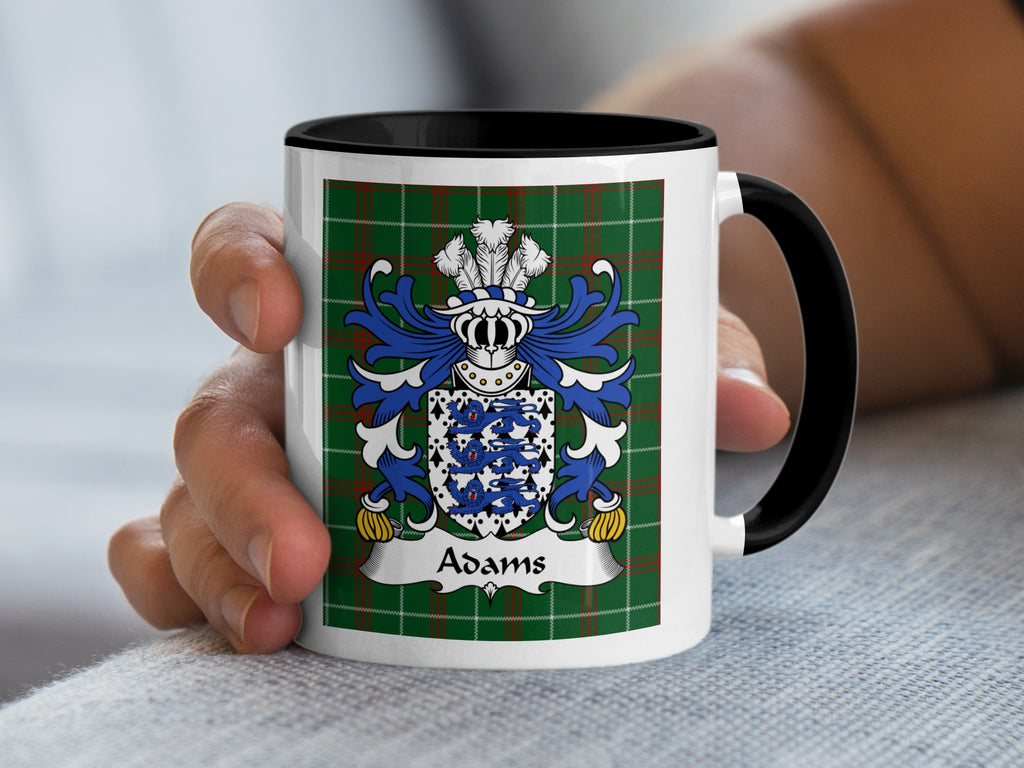 White mug with black handle and rim, featuring the Adams family crest on a green tartan background.