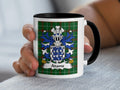 White mug with black handle and rim, featuring the Adams family crest on a green tartan background.