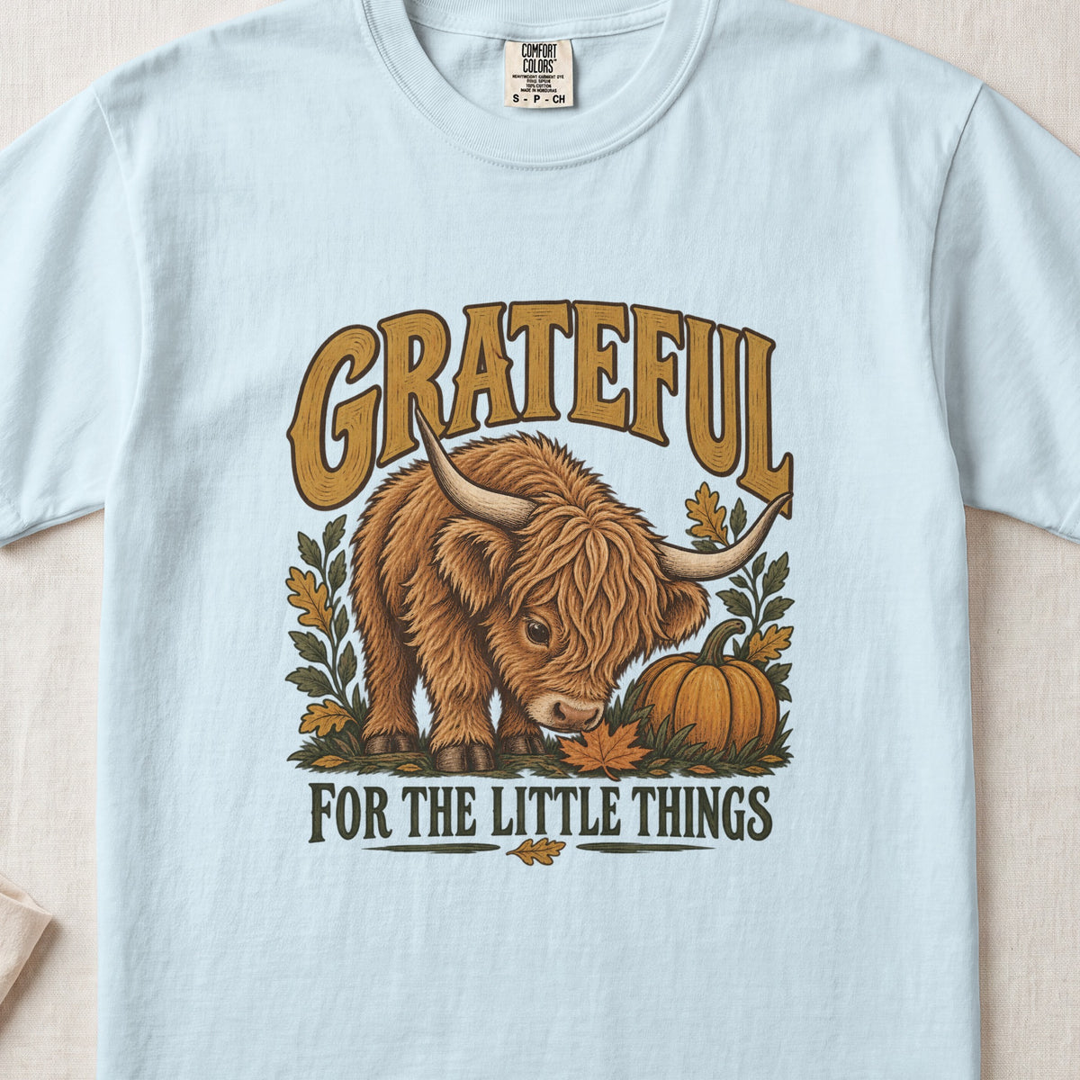 Grateful for the Little Things Highland cow design on a Chambray Comfort Colors 1717 T-shirt, flat lay