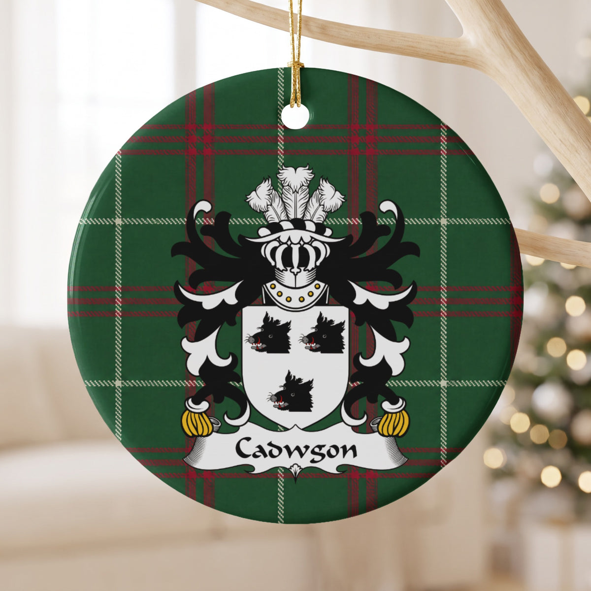 Cadwgon Style 1 ornament hanging from a pale wooden branch; three black boar heads on a white shield on Welsh national tartan.