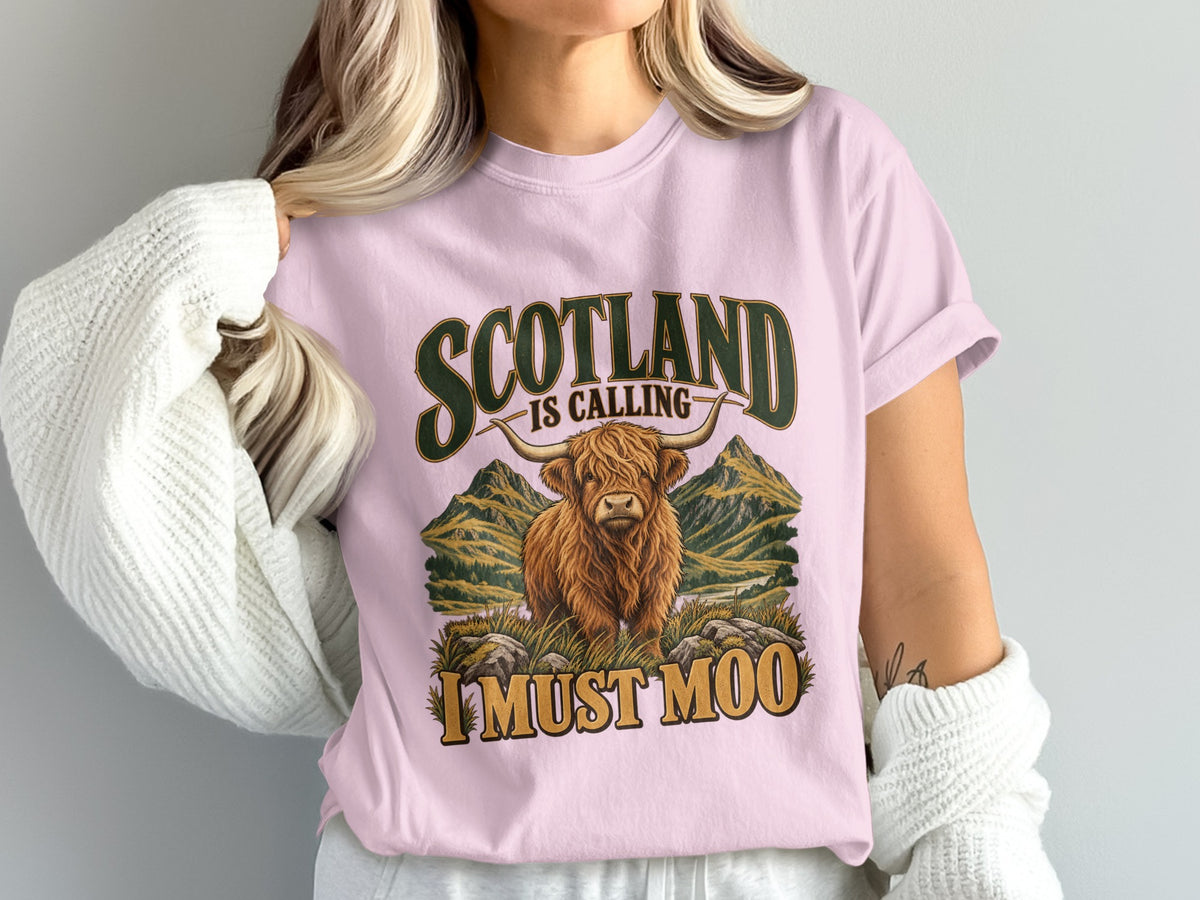 Model wearing the Scotland Is Calling, I Must Moo Highland cow Comfort Colors T-shirt in Blossom