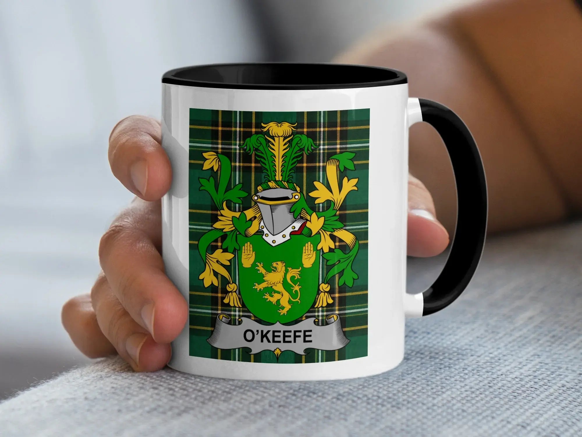 White mug with black rim displaying O'KEEFE family crest on plaid background.
