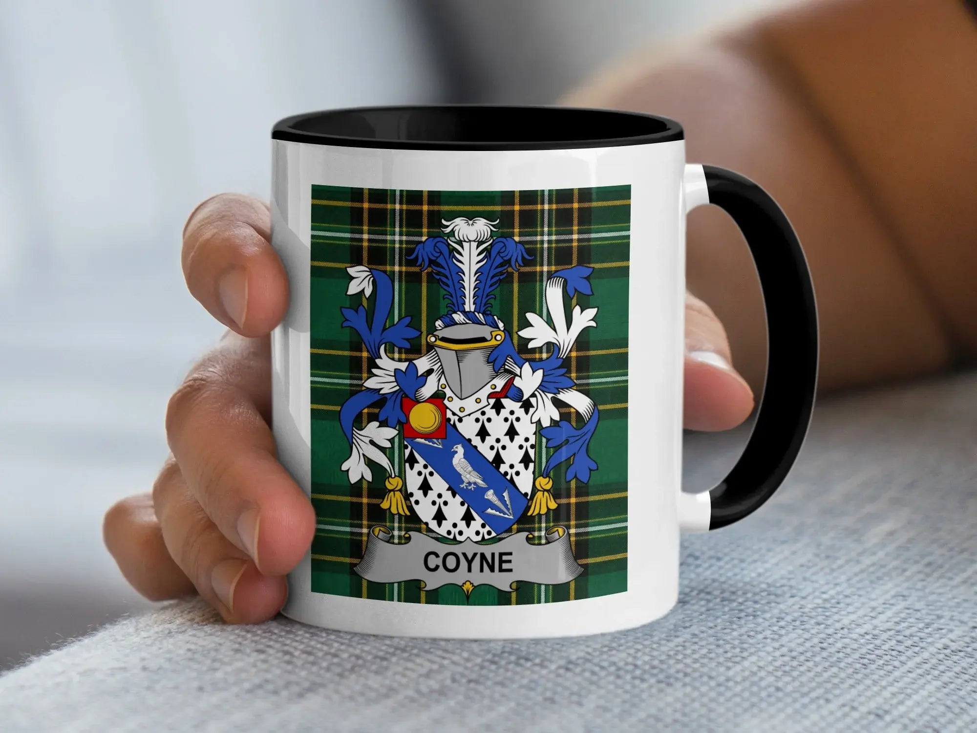 Mug with black handle and white ceramic body displaying a blue and white coat of arms with the surname COYNE.