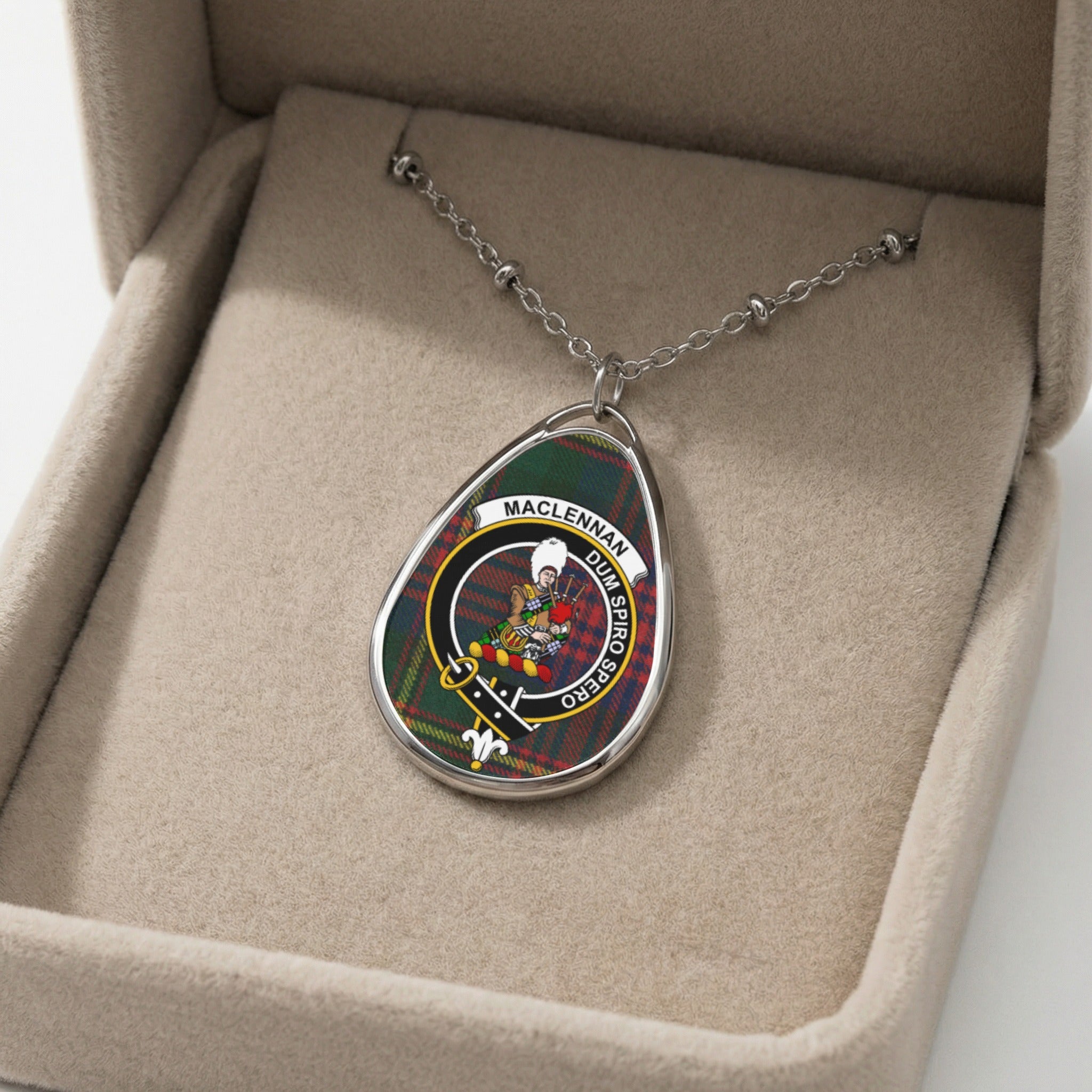 Silver oval pendant with MacLennan clan crest and motto on tartan background.