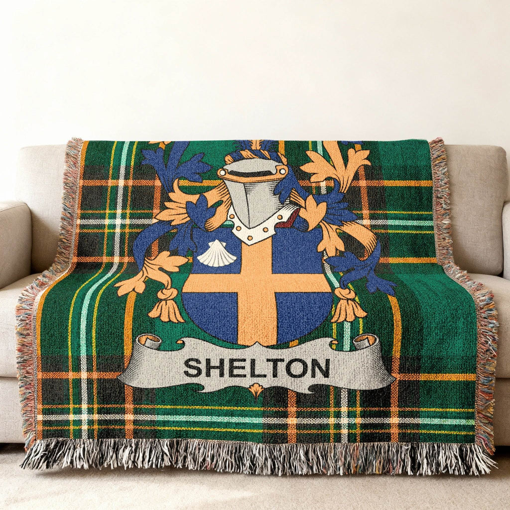 Woven blanket with Shelton family crest and tartan pattern on a sofa.