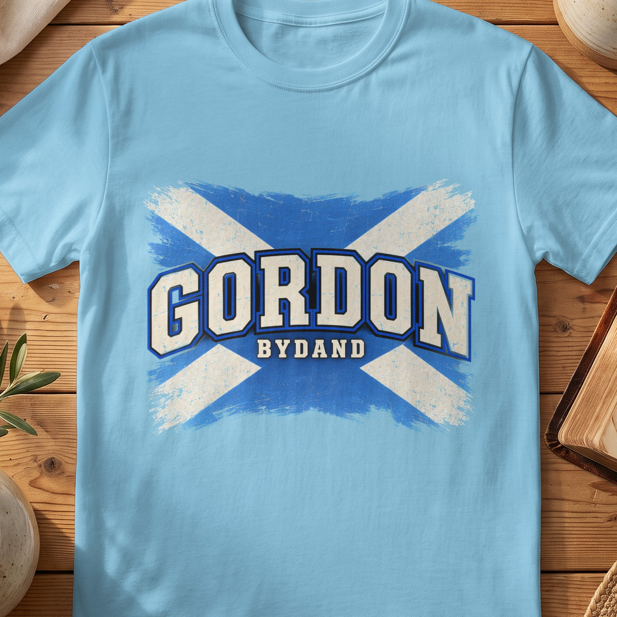 Gordon Scottish Saltire T-shirt in Sky, with distressed blue and cream flag and “Bydand” lettering.