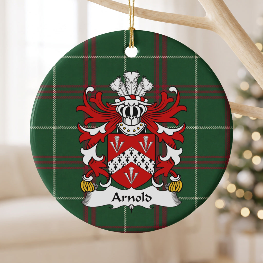 Arnold family crest and surname on a round Welsh national tartan ornament, hanging by a gold cord from a pale wooden branch with blurred Christmas lights behind it.