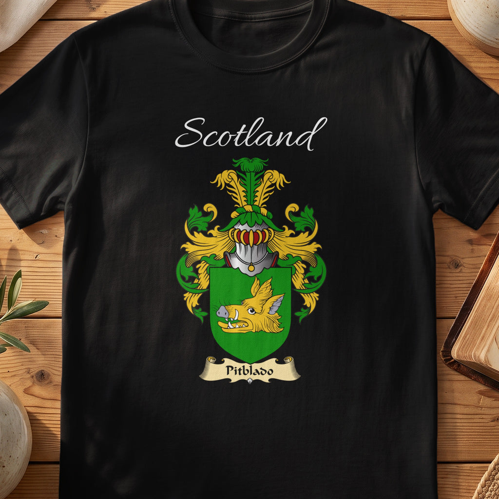 Black Pitblado Scottish family crest T-shirt laid flat, showing “Scotland” above a green-and-gold shield carrying a gold bird-like figure.