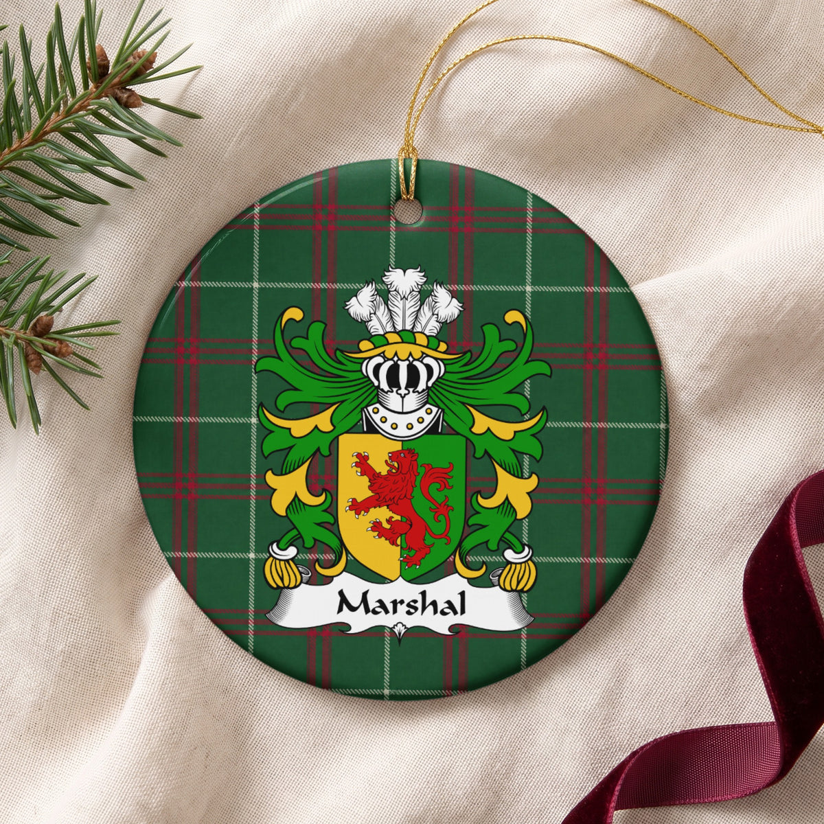 Marshal ornament on cream fabric with gold string, evergreen and burgundy ribbon; a red lion on a gold-and-green divided shield on Welsh National Tartan.