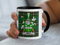 White mug with black rim, featuring a green tartan and a coat of arms with the name WELD.