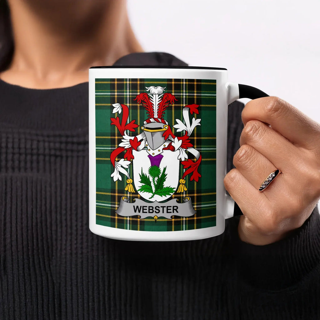 Mug with Webster family crest on green plaid background, held by a hand.