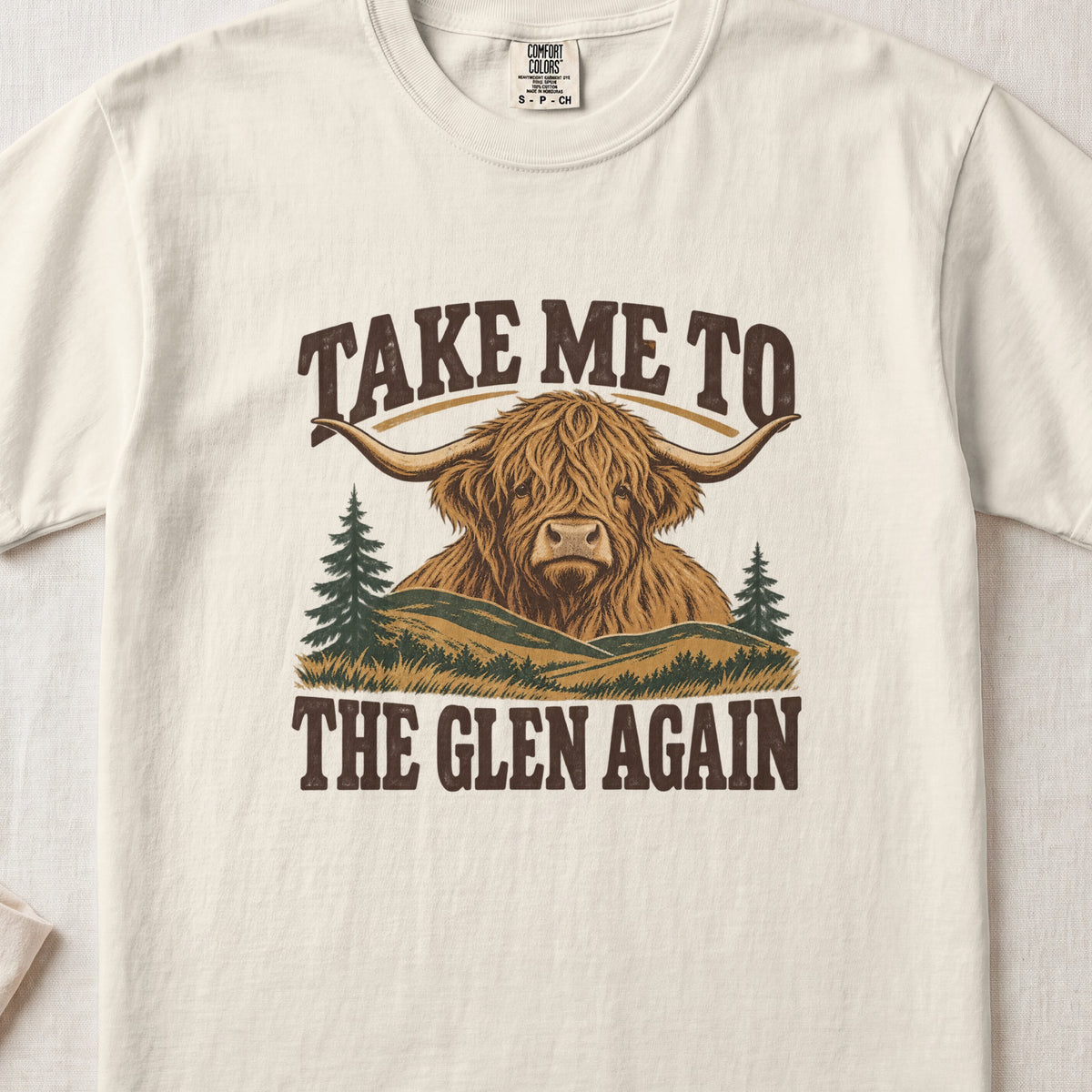 Take Me to the Glen Again Highland cow design on an Ivory Comfort Colors 1717 T-shirt, flat lay