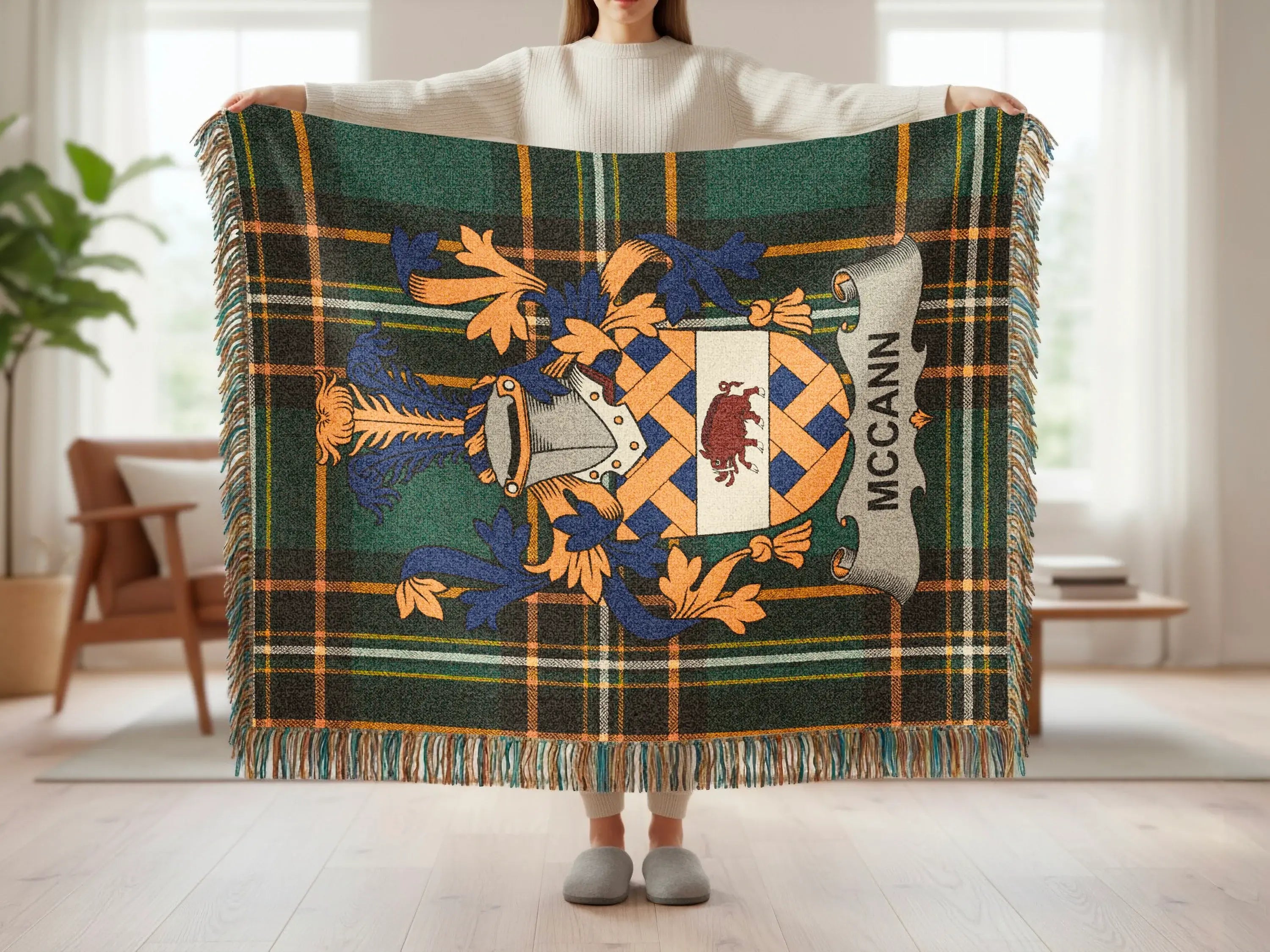 Tartan throw blanket with McCann family crest held by person.