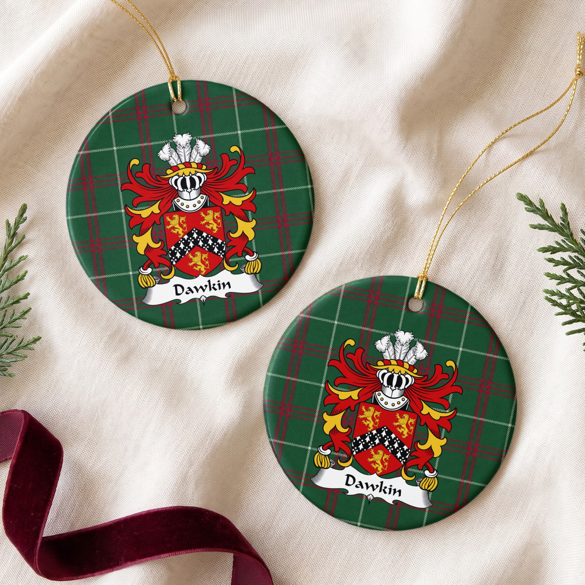 Two Dawkin ornaments on cream fabric beside evergreen and burgundy ribbon; three gold lions around a black chevron with white ermine-style markings on red.