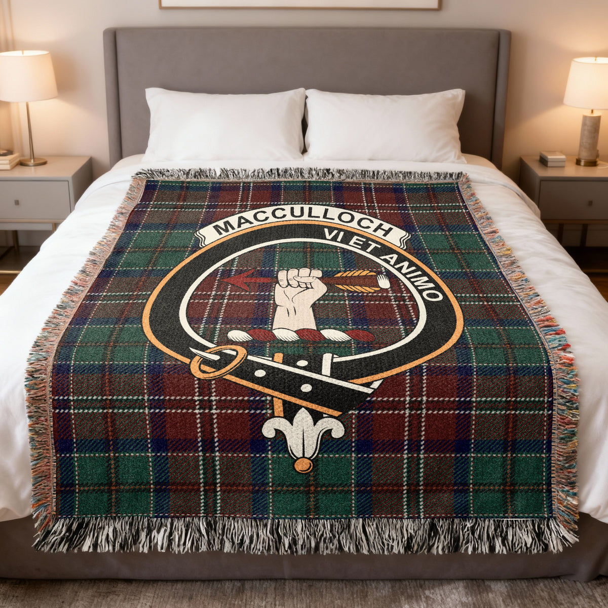 MacCulloch woven blanket displayed on a bed, with a hand holding a dart on a green, burgundy and blue tartan background