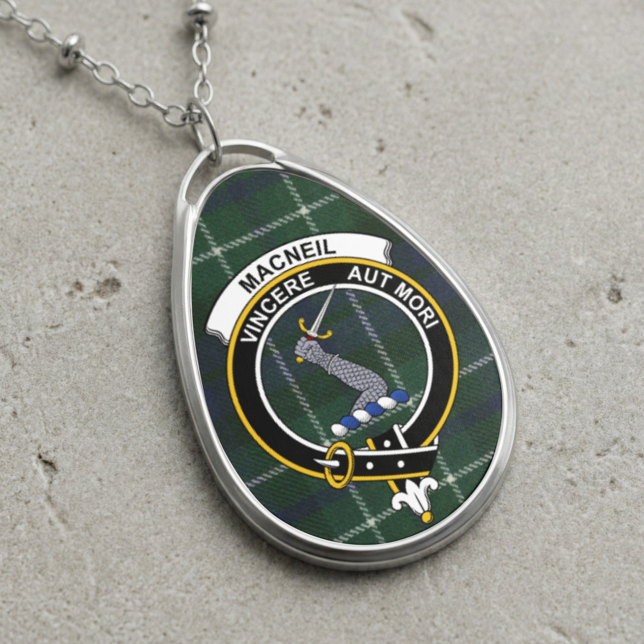 Macneil clan crest pendant on a silver chain with plaid background and "Vincere Aut Mori" motto.