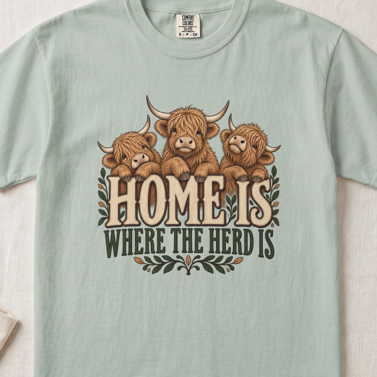 Home Is Where the Herd Is Highland cow design on a Bay Comfort Colors 1717 T-shirt, flat lay