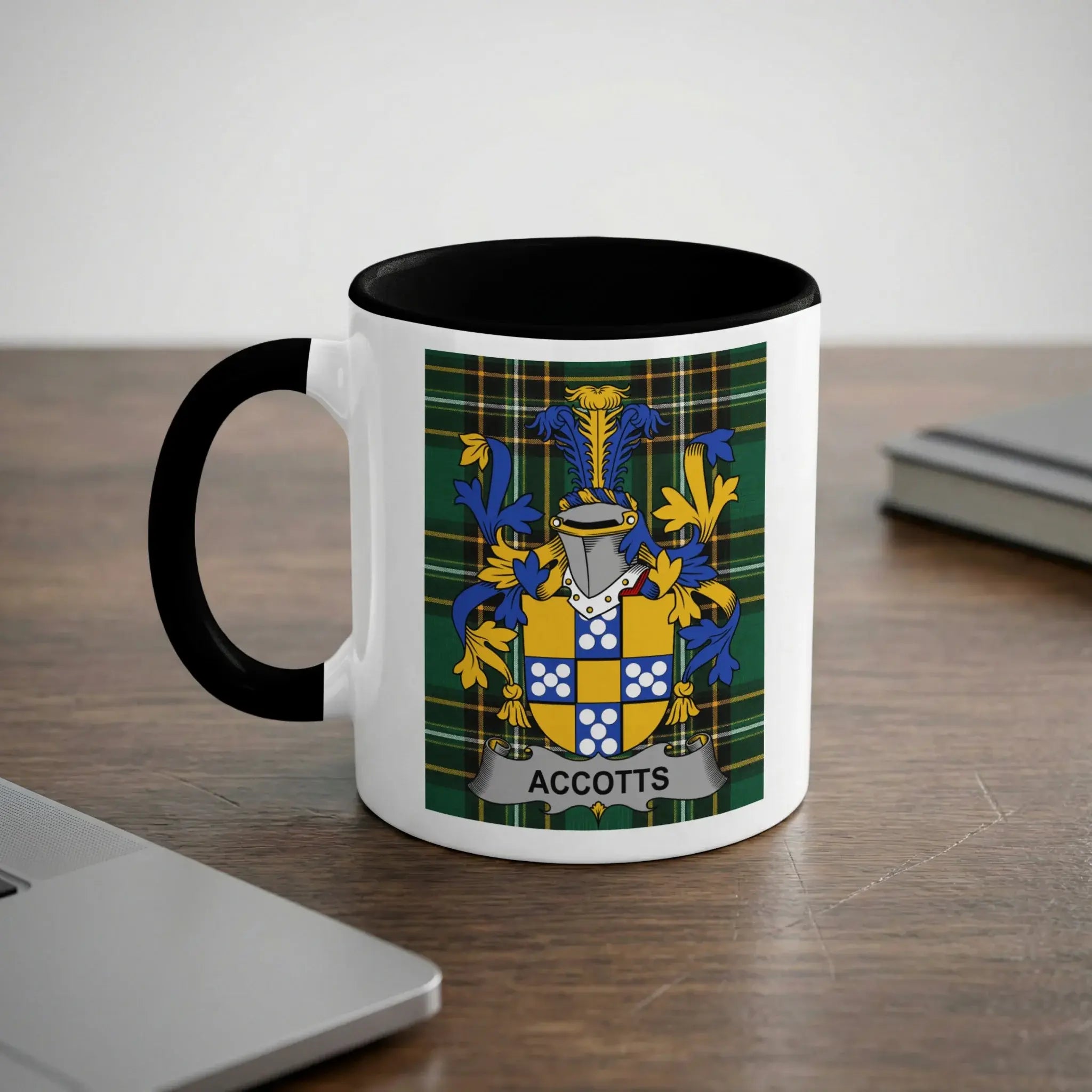 White mug with black rim and handle featuring the "ACCOTTS" coat of arms on plaid background.