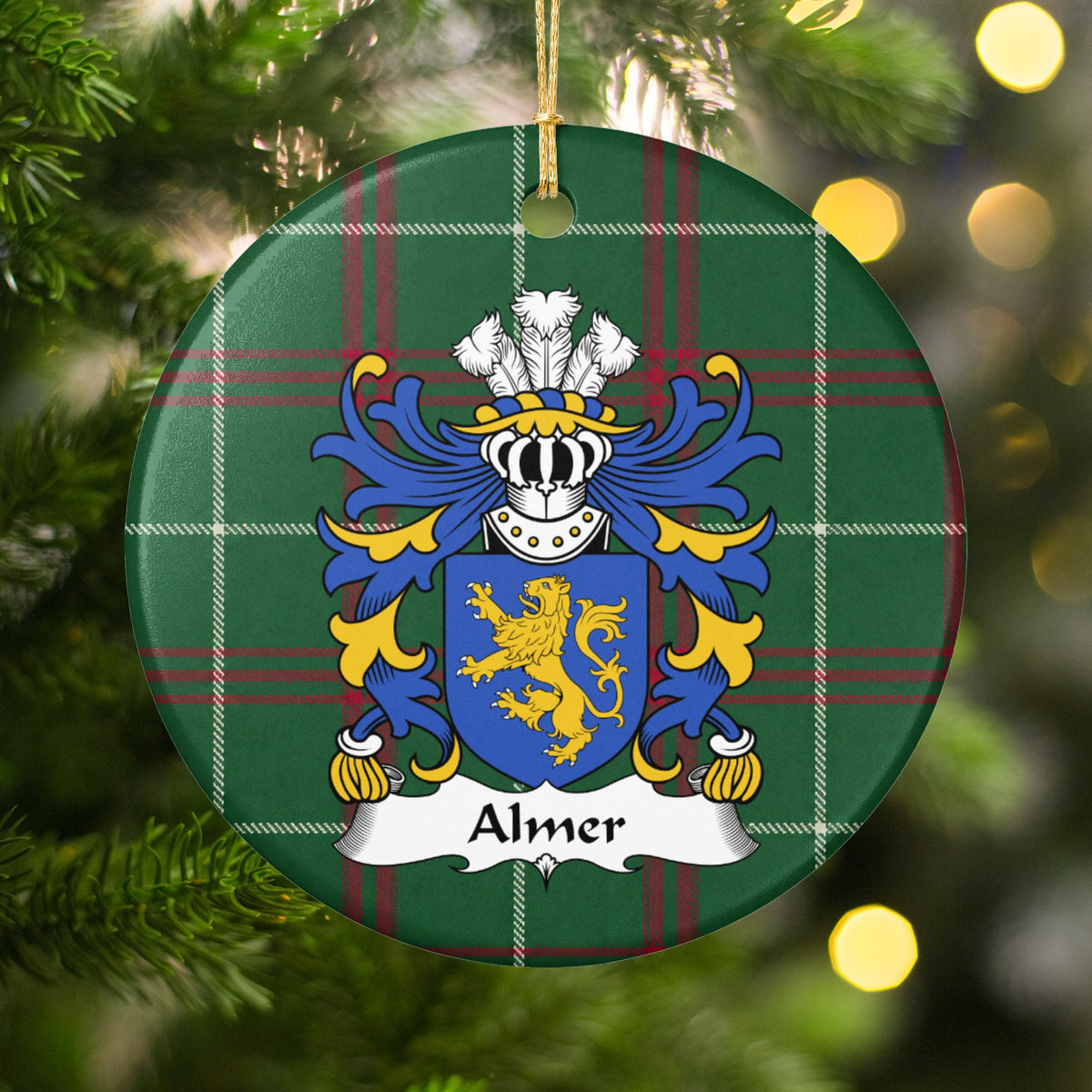 Almer family crest and surname on a round Welsh national tartan ornament, hanging by a gold cord among Christmas tree branches and warm golden lights.