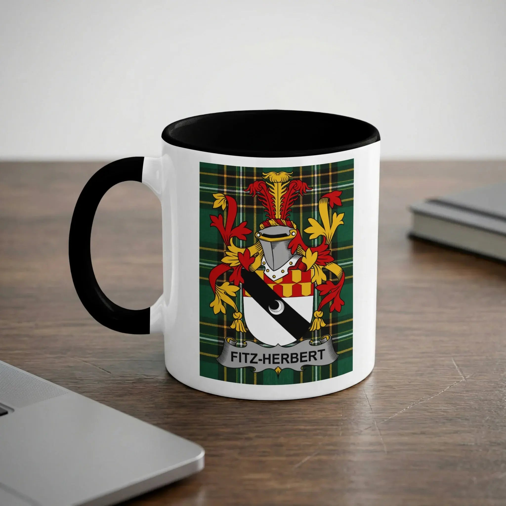 Mug with Fitz-Herbert family crest on wood desk beside laptop.
