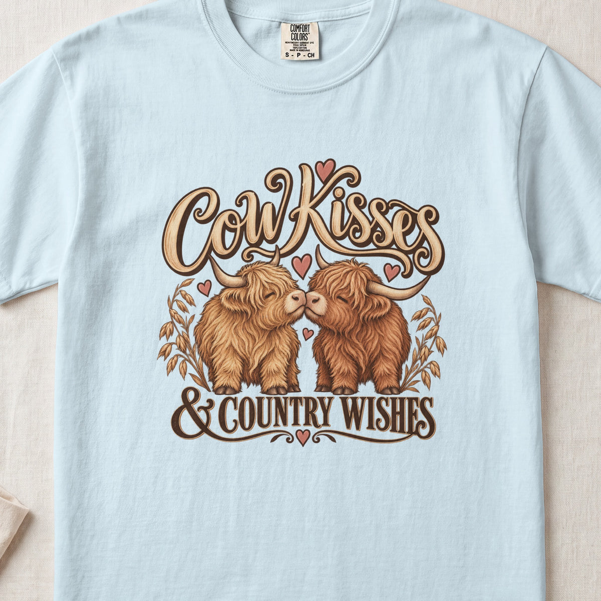 Cow Kisses & Country Wishes Highland cow design on a Chambray Comfort Colors 1717 T-shirt, flat lay