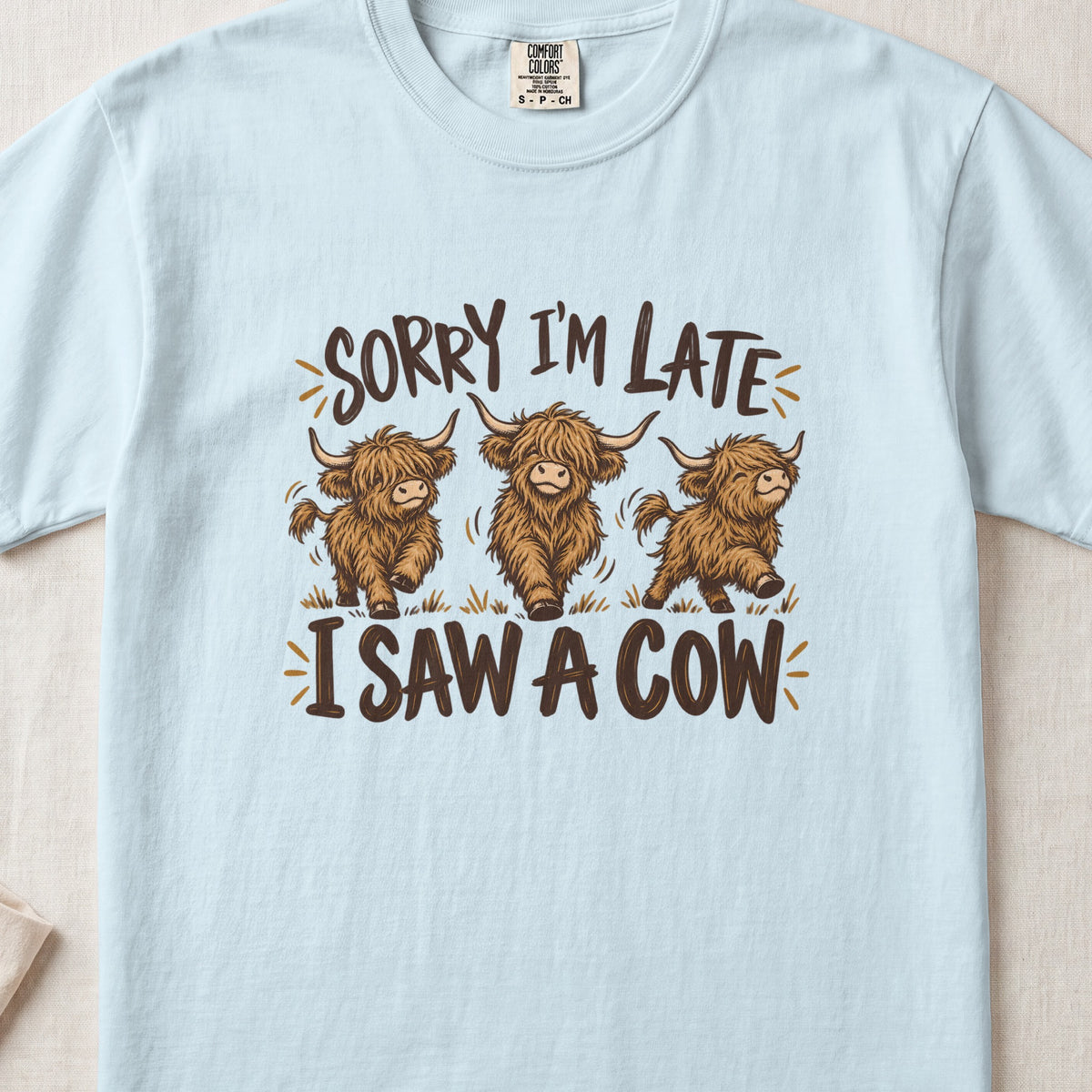 Sorry I'm Late, I Saw a Cow Highland cow design on a Chambray Comfort Colors 1717 T-shirt, flat lay