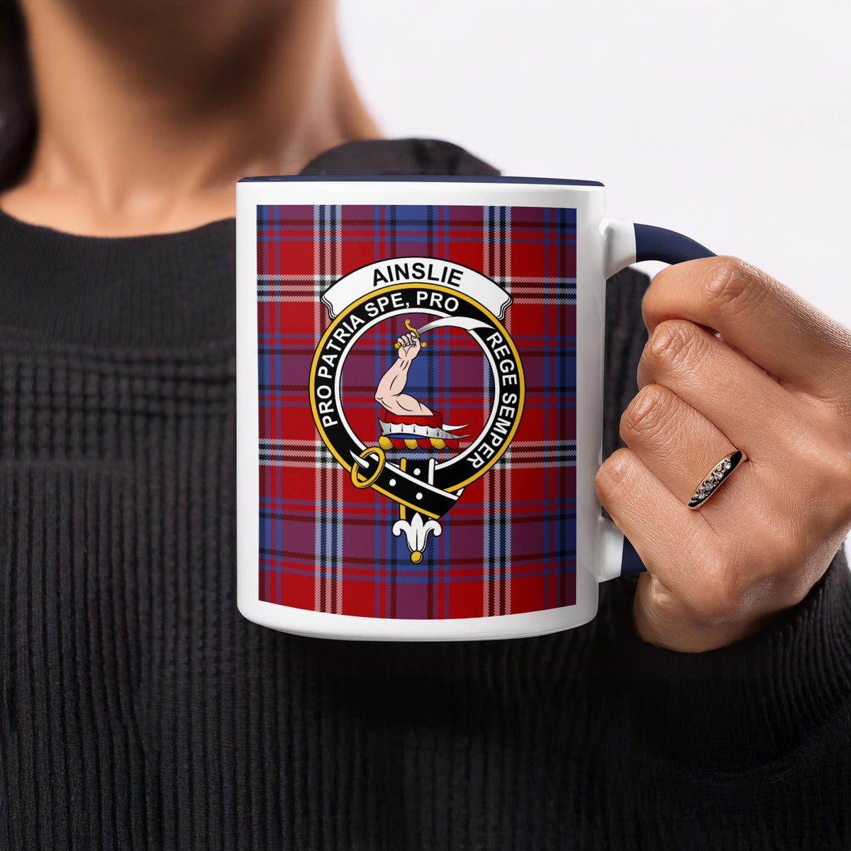 Close-up lifestyle view of Ainslie Scottish family crest artwork on a navy 11 oz accent mug with a tartan background