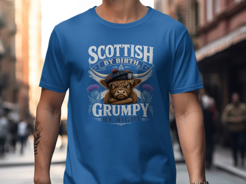 Blue t-shirt with a grumpy Highland cow wearing a tartan tam, text "Scottish by Birth, Grumpy by Right".