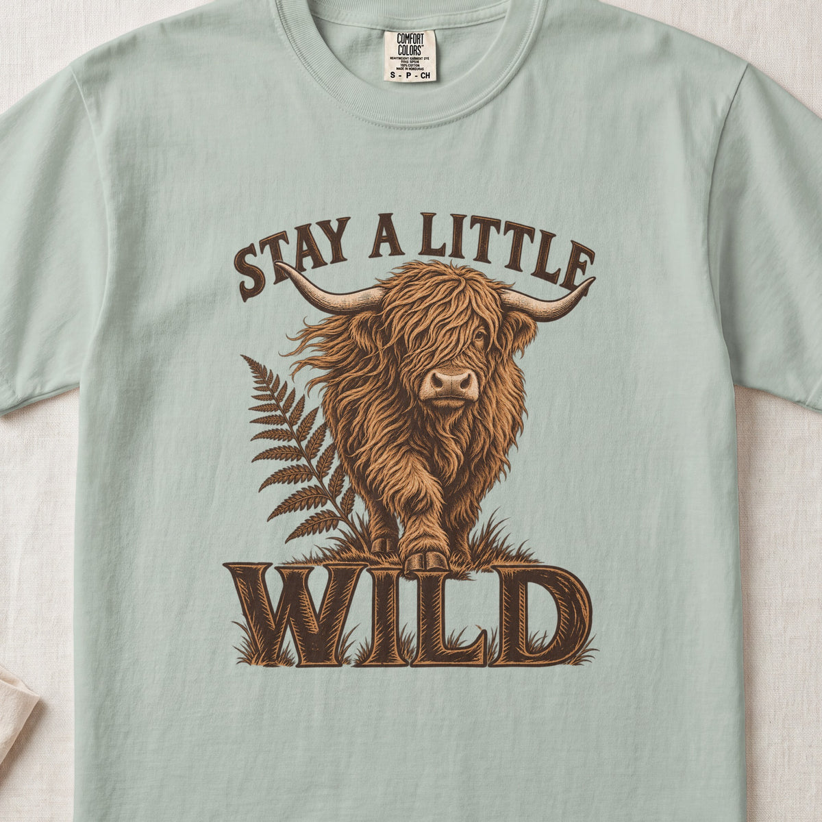 Stay a Little Wild Highland cow design on a Bay Comfort Colors 1717 T-shirt, flat lay