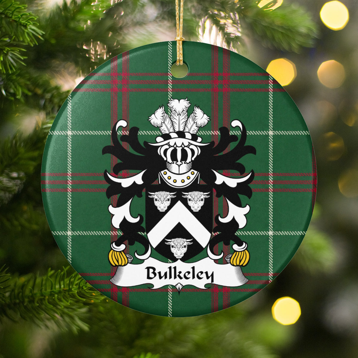 Bulkeley ornament hanging in a Christmas tree with warm lights; a white chevron between three white bull heads on black on Welsh national tartan.