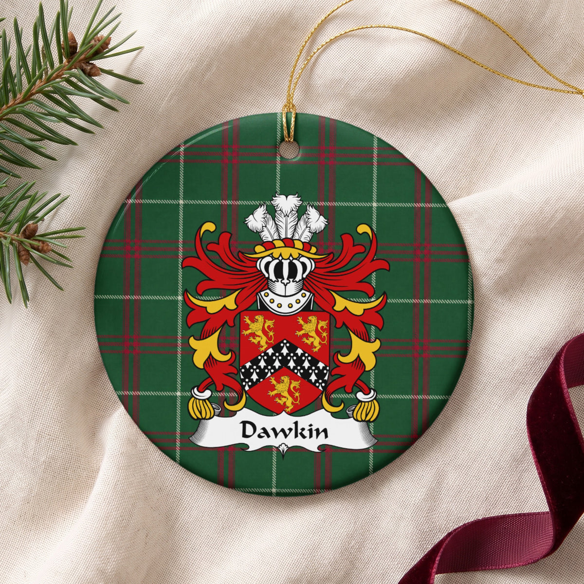 Dawkin ornament on cream fabric with gold string, evergreen and burgundy ribbon; three gold lions around a black chevron with white ermine-style markings on red.