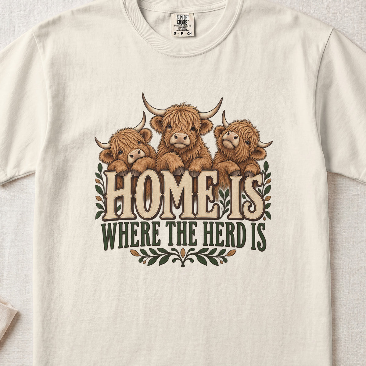 Home Is Where the Herd Is Highland cow design on an Ivory Comfort Colors 1717 T-shirt, flat lay