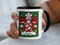 Black-accent Hughes mug held in a hand, showing a red-and-silver shield on a tartan background.