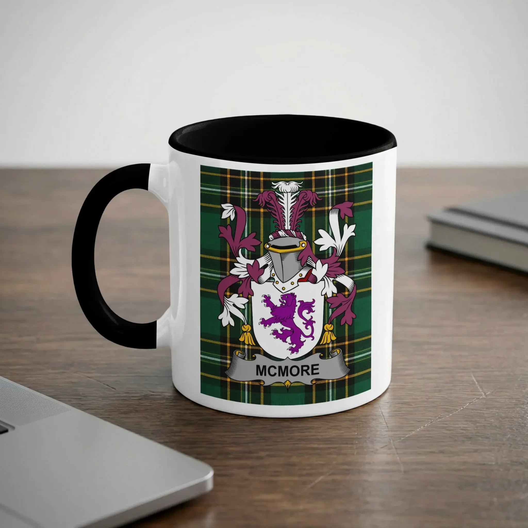 White mug with black handle and rim displaying the McMore family crest on a tartan background.