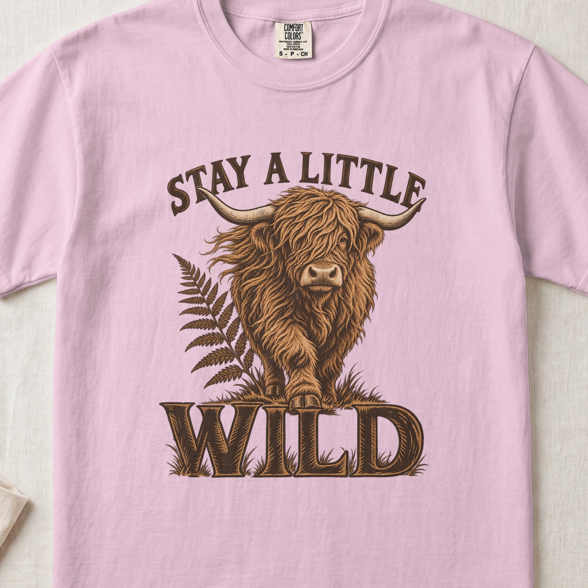 Stay a Little Wild Highland cow design on a Blossom Comfort Colors 1717 T-shirt, flat lay