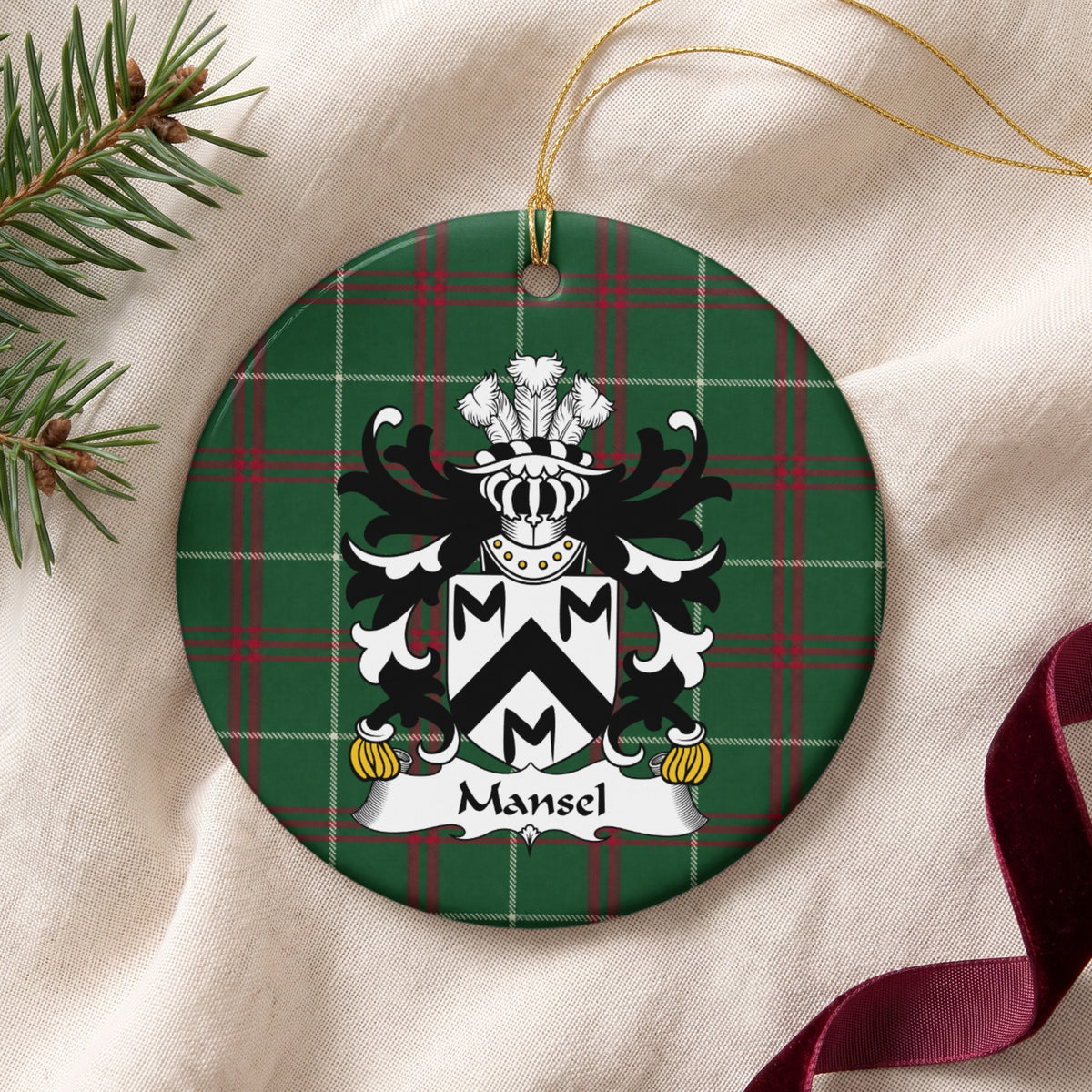 Mansel ornament on cream fabric with gold string, evergreen and burgundy ribbon; a black chevron and three black M-shaped motifs on a white shield on Welsh National Tartan.