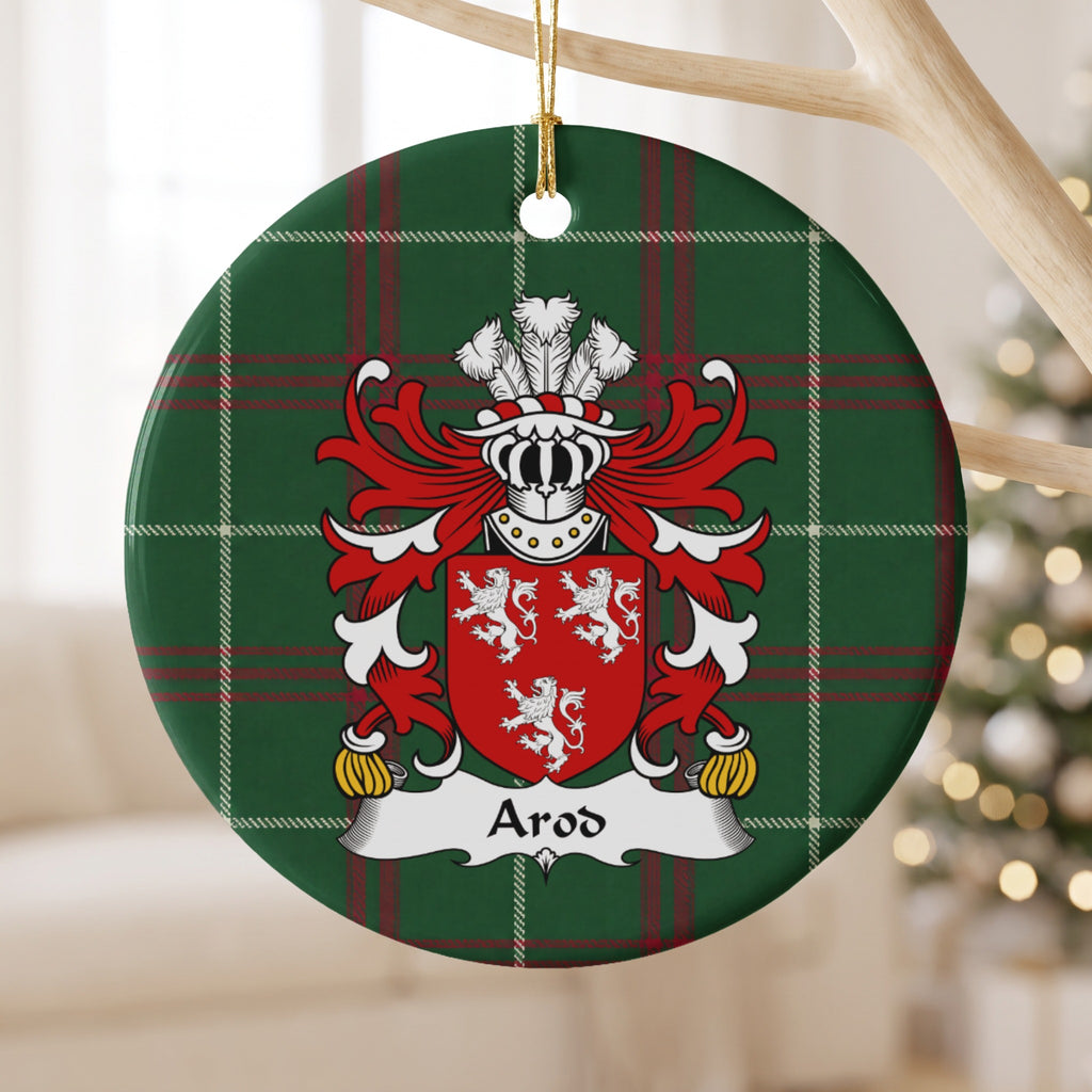 Arod family crest and surname on a round Welsh national tartan ornament, hanging by a gold cord from a pale wooden branch with blurred Christmas lights behind it.