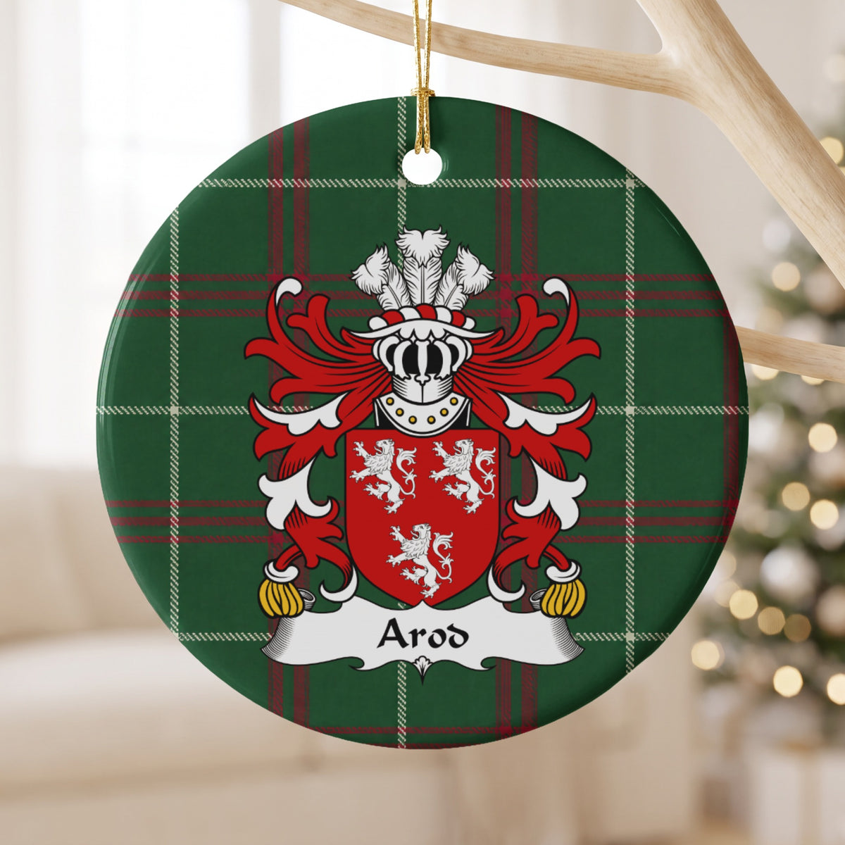 Arod family crest and surname on a round Welsh national tartan ornament, hanging by a gold cord from a pale wooden branch with blurred Christmas lights behind it.