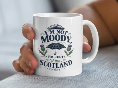 White mug with "I'm not moody, I'm just from Scotland" and plaid umbrella design.